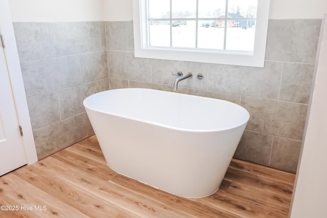 bathroom featuring a tub to relax in, hardwood / wood-style floors, and tile walls