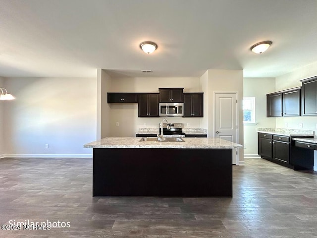 kitchen featuring sink, dark hardwood / wood-style floors, light stone countertops, an island with sink, and stainless steel appliances