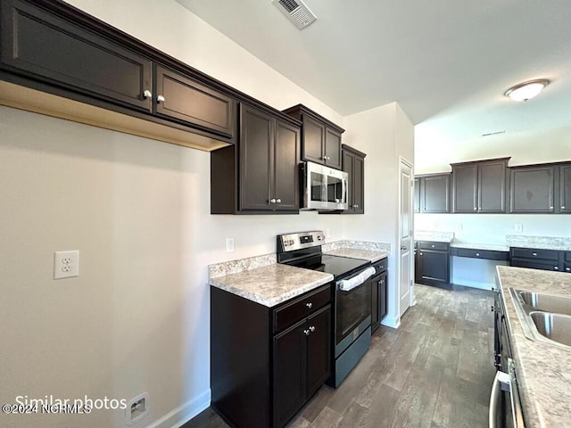 kitchen with dark brown cabinets, dark hardwood / wood-style flooring, light stone counters, and appliances with stainless steel finishes