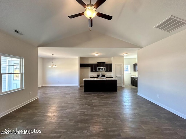 kitchen featuring appliances with stainless steel finishes, ceiling fan with notable chandelier, a kitchen island with sink, dark wood-type flooring, and hanging light fixtures