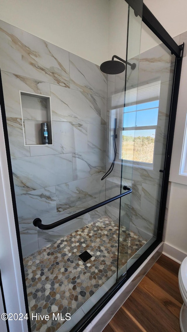 bathroom with wood-type flooring, toilet, and a shower with shower door