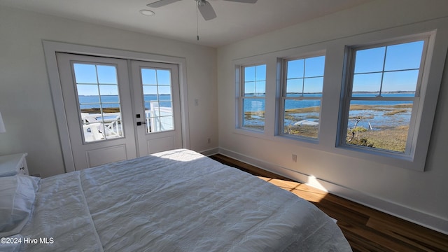 bedroom with dark wood-type flooring, access to outside, french doors, a water view, and ceiling fan