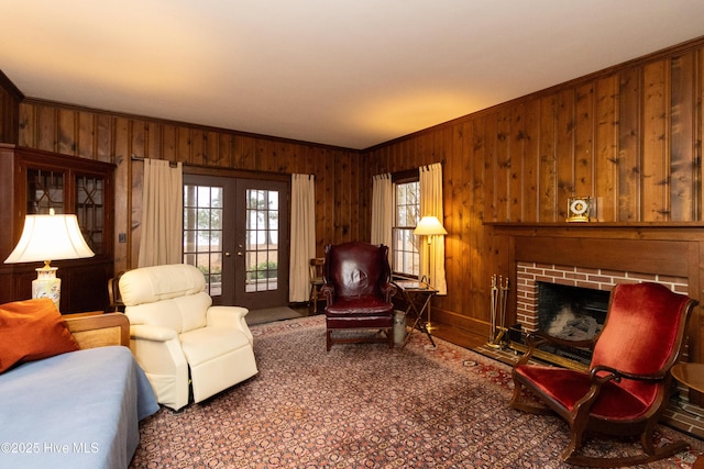 living room featuring wooden walls, french doors, ornamental molding, and a brick fireplace