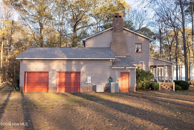 exterior space with a sunroom, central AC unit, a garage, and a lawn