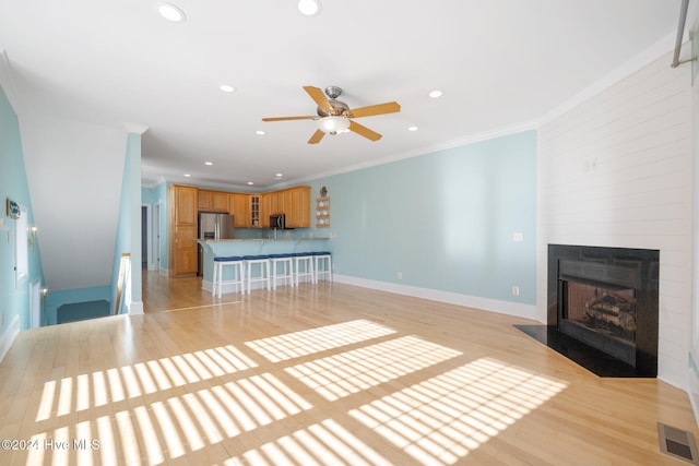 unfurnished living room with crown molding, light hardwood / wood-style floors, a large fireplace, and ceiling fan