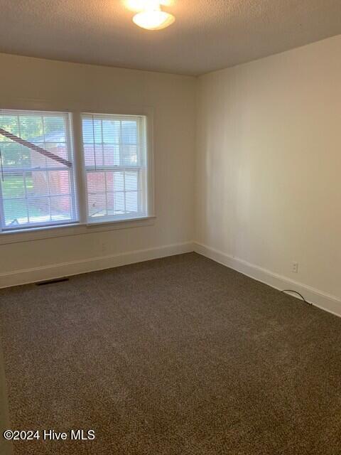 unfurnished room featuring dark colored carpet and a textured ceiling