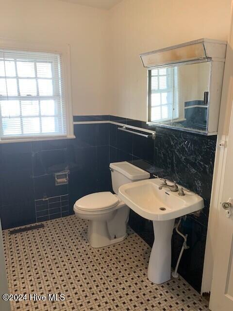 bathroom with tile patterned flooring, toilet, and tile walls