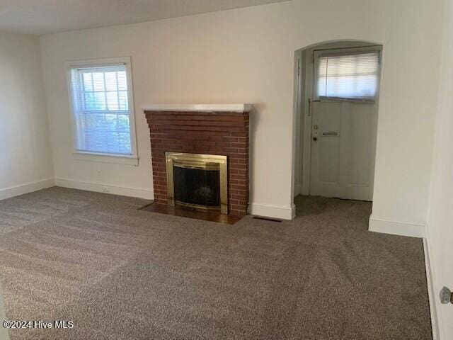 unfurnished living room with dark colored carpet and a brick fireplace