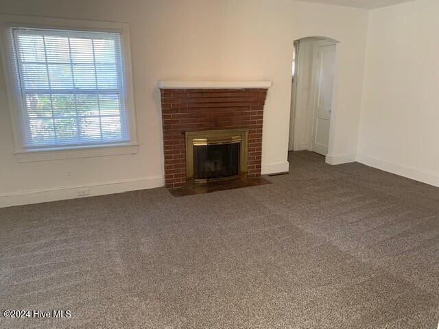 unfurnished living room with dark colored carpet and a brick fireplace