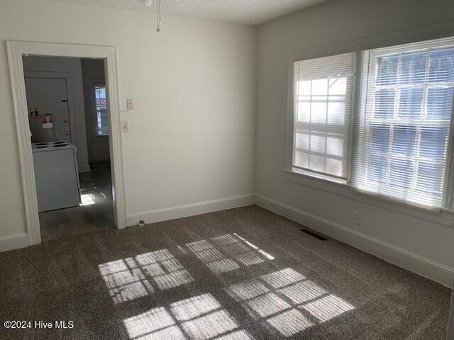 empty room with washer / clothes dryer, ceiling fan, and dark carpet