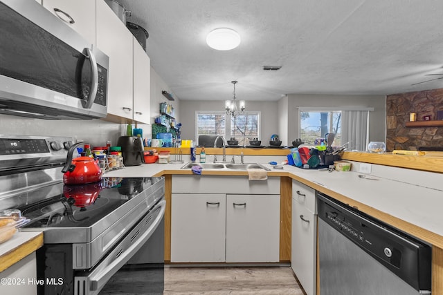 kitchen featuring appliances with stainless steel finishes, a textured ceiling, decorative light fixtures, a chandelier, and white cabinetry