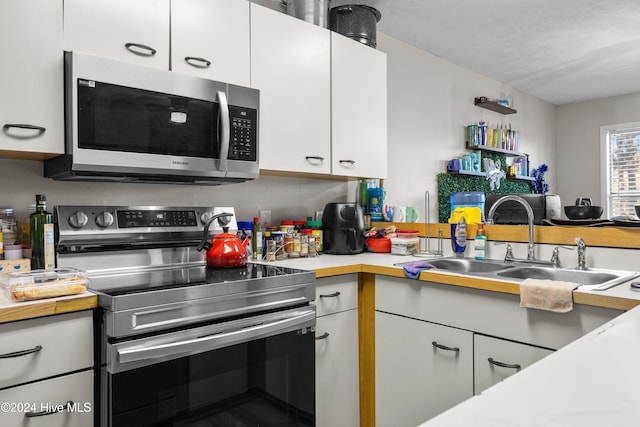 kitchen with white cabinets, appliances with stainless steel finishes, a textured ceiling, and sink