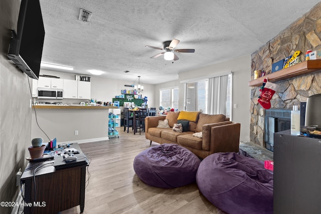 living room with ceiling fan, a fireplace, light hardwood / wood-style floors, and a textured ceiling