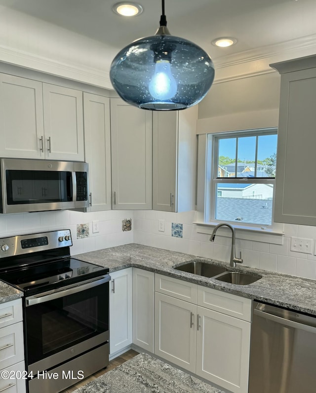 kitchen with sink, light stone counters, backsplash, pendant lighting, and appliances with stainless steel finishes