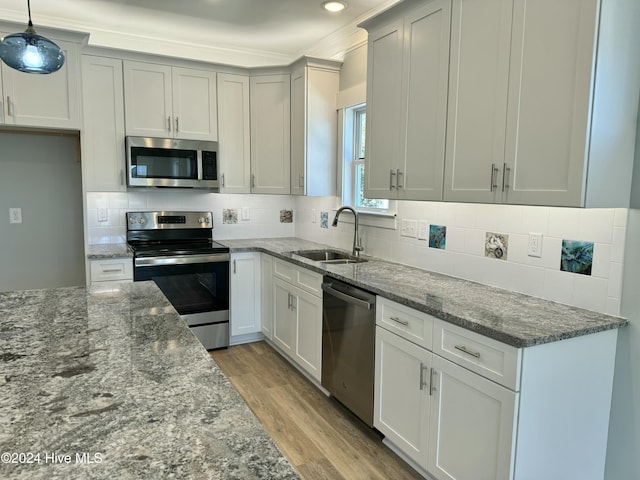 kitchen featuring sink, hanging light fixtures, stone countertops, appliances with stainless steel finishes, and light wood-type flooring