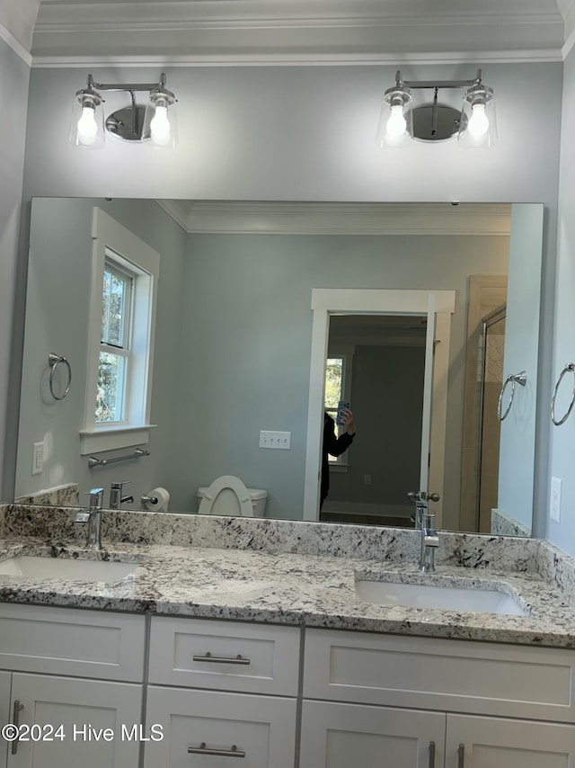 bathroom with vanity, toilet, a shower with shower door, and crown molding