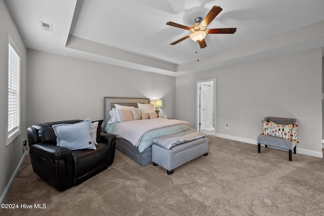 bedroom featuring a raised ceiling, multiple windows, ceiling fan, and light carpet