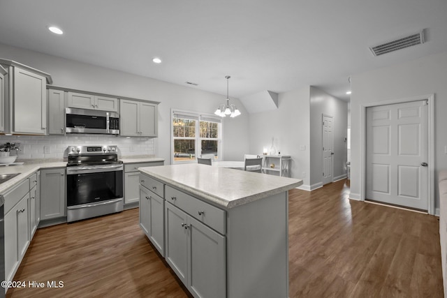 kitchen featuring appliances with stainless steel finishes, tasteful backsplash, pendant lighting, a notable chandelier, and a center island