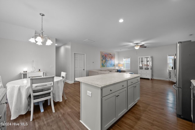 kitchen featuring stainless steel fridge, dark hardwood / wood-style flooring, ceiling fan with notable chandelier, pendant lighting, and a kitchen island