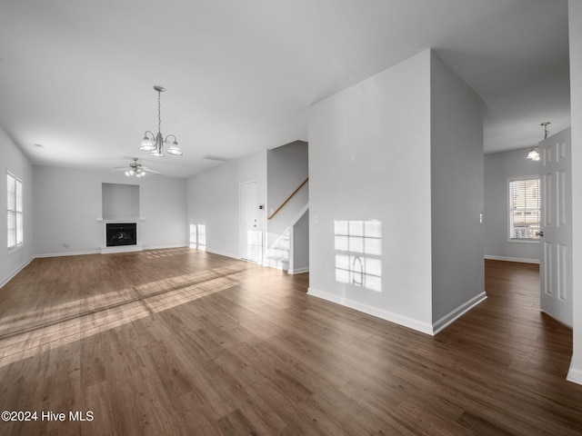 unfurnished living room with ceiling fan with notable chandelier and dark hardwood / wood-style flooring