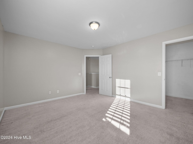 unfurnished bedroom with light colored carpet, a spacious closet, and a closet