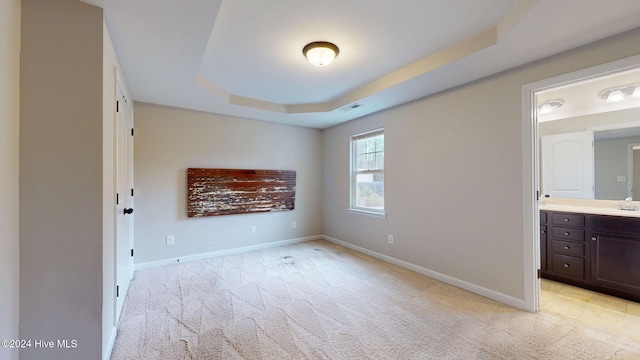 unfurnished bedroom with a raised ceiling, ensuite bathroom, sink, and light carpet