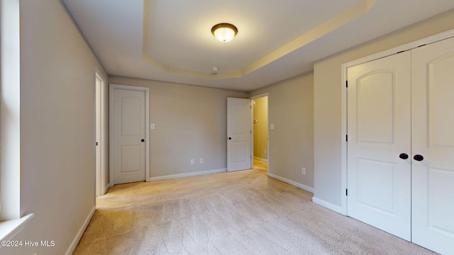 unfurnished bedroom with light carpet, a tray ceiling, and a closet