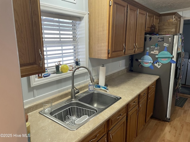 kitchen featuring a textured ceiling, light hardwood / wood-style floors, stainless steel refrigerator, and sink