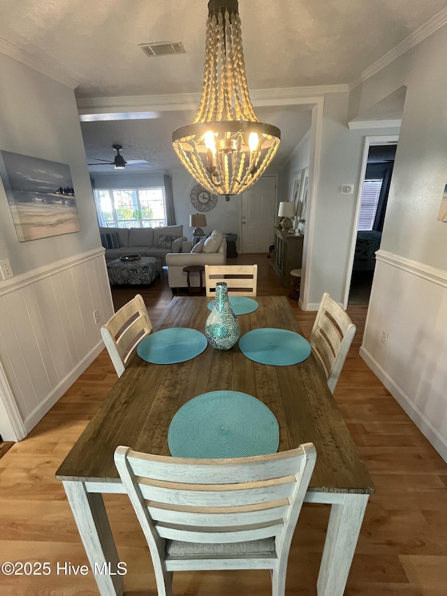 dining area with ceiling fan with notable chandelier, wood-type flooring, and ornamental molding