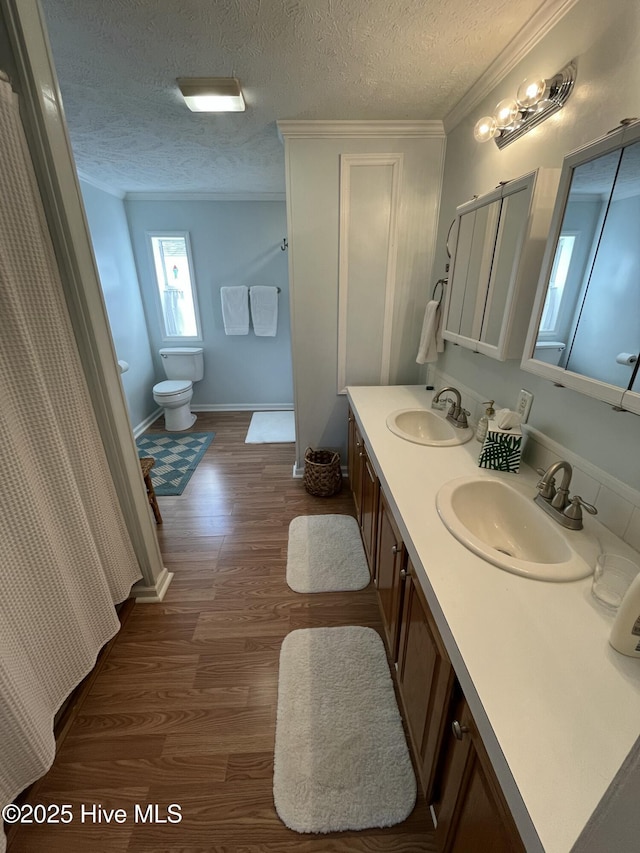 bathroom featuring wood-type flooring, a textured ceiling, toilet, vanity, and ornamental molding