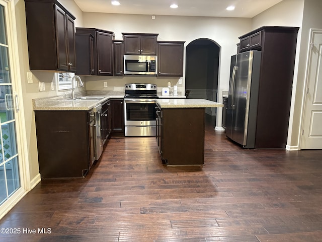 kitchen featuring sink, light stone countertops, appliances with stainless steel finishes, a kitchen island, and dark hardwood / wood-style flooring