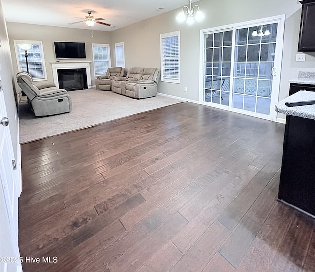 living room featuring ceiling fan with notable chandelier and dark wood-type flooring