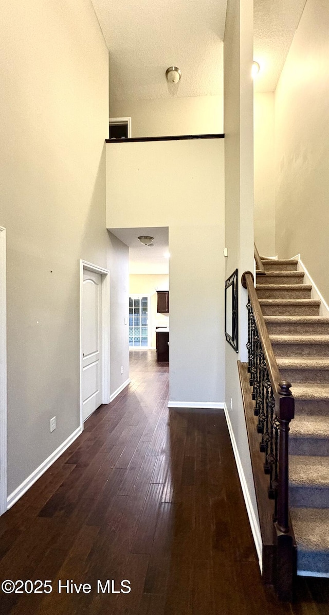 stairs featuring a textured ceiling, a high ceiling, and hardwood / wood-style flooring