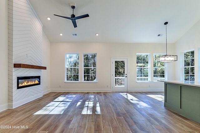 unfurnished living room with a large fireplace, visible vents, lofted ceiling, wood finished floors, and ceiling fan with notable chandelier