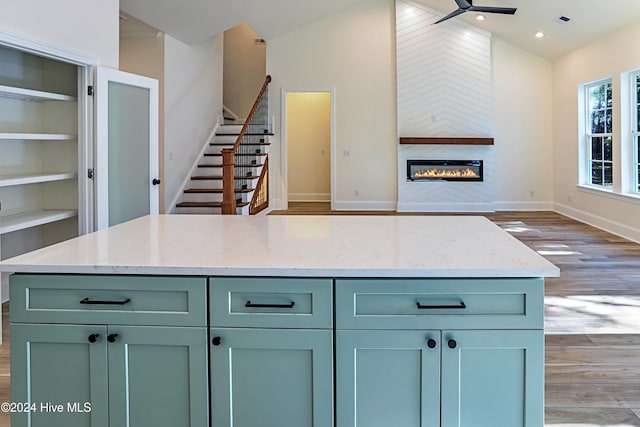 kitchen with light stone counters, lofted ceiling, light wood-style flooring, a glass covered fireplace, and baseboards