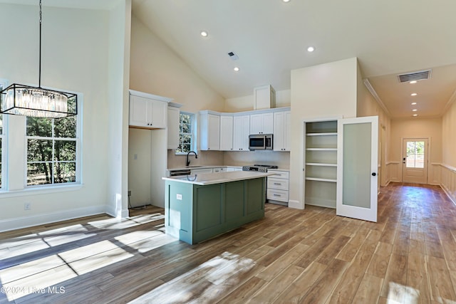 kitchen with visible vents, light wood-style flooring, stainless steel microwave, light countertops, and white cabinetry