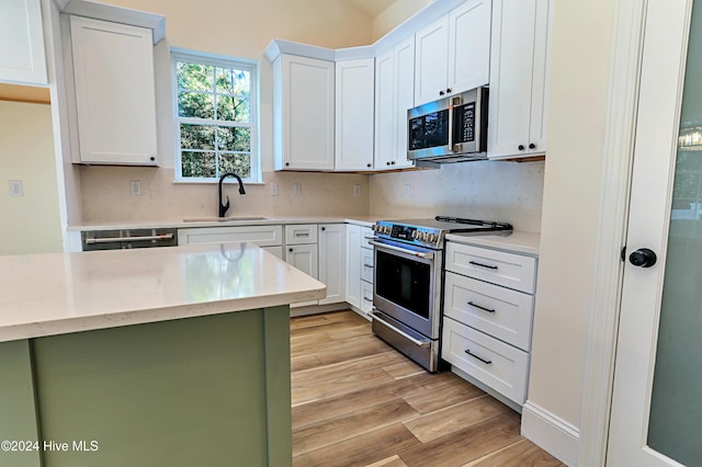 kitchen with a sink, white cabinets, appliances with stainless steel finishes, light wood-type flooring, and backsplash