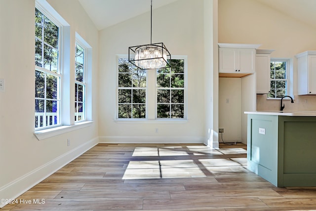 unfurnished dining area featuring baseboards, light wood-style flooring, a notable chandelier, vaulted ceiling, and a sink