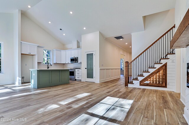 kitchen featuring a kitchen island with sink, high vaulted ceiling, white cabinets, appliances with stainless steel finishes, and decorative light fixtures