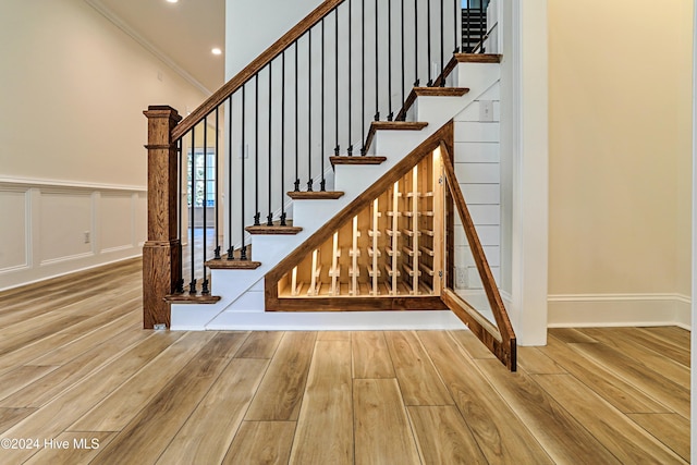 staircase featuring a wainscoted wall, crown molding, a decorative wall, and wood finished floors