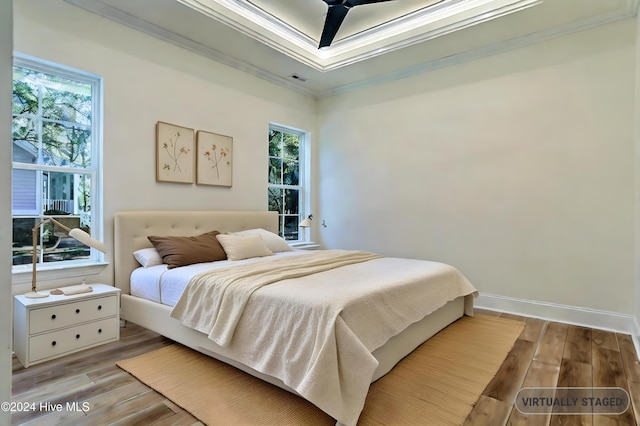 bedroom featuring baseboards, visible vents, ornamental molding, wood finished floors, and a tray ceiling