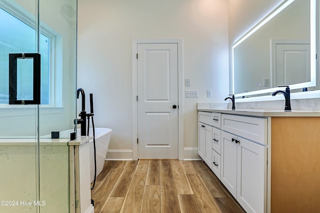 full bath featuring a soaking tub, vanity, baseboards, and wood finished floors