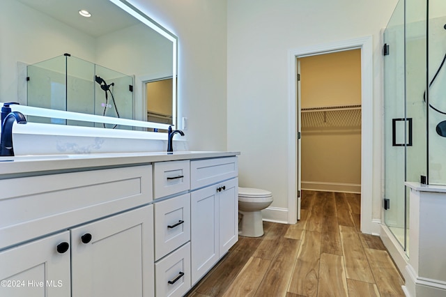 bathroom with toilet, wood finished floors, a spacious closet, vanity, and a shower stall