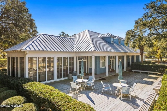 back of property with outdoor dining space, a sunroom, a standing seam roof, metal roof, and a deck