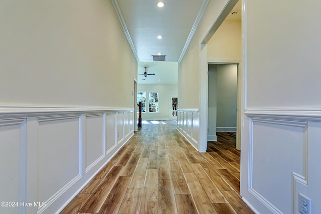 hallway with visible vents, a decorative wall, ornamental molding, wainscoting, and wood finished floors