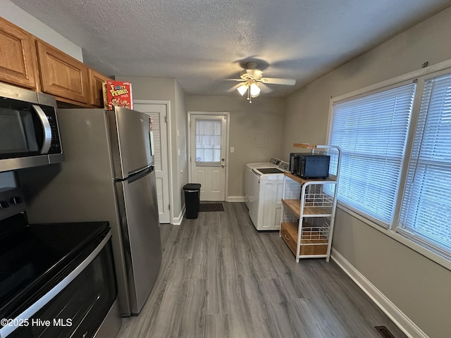 kitchen with range with electric cooktop, light hardwood / wood-style flooring, ceiling fan, a textured ceiling, and washer / clothes dryer