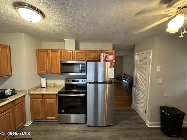 kitchen with ceiling fan, dark wood-type flooring, light stone counters, a textured ceiling, and appliances with stainless steel finishes