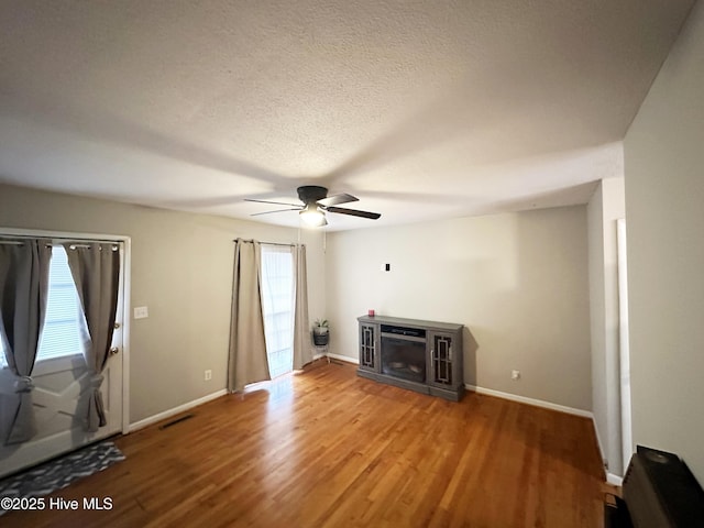 unfurnished living room featuring a fireplace, wood-type flooring, a textured ceiling, and ceiling fan