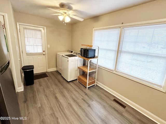 laundry room featuring washing machine and clothes dryer, a wealth of natural light, ceiling fan, and wood-type flooring