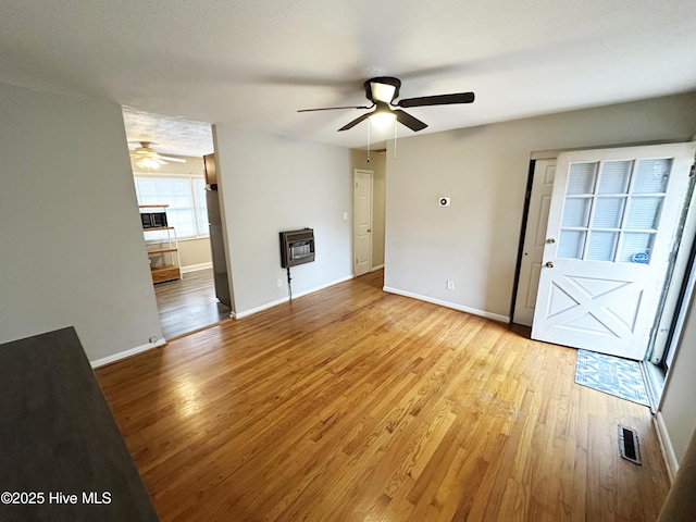 unfurnished living room with heating unit, ceiling fan, and light hardwood / wood-style flooring